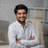 Confident young Indian businessman sitting on edge of his table and looking at camera
